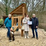 Marion Klein (Geschäftsführerin) und Eva Weil (Regionalmanagerin) von der Region Lahn-Dill-Bergland e. V. bei der Übergabe des Projektschild zur erhaltenen Förderung an Michael Lotz. Der geförderte Krabbelturm ist hinter den Personen zu sehen.