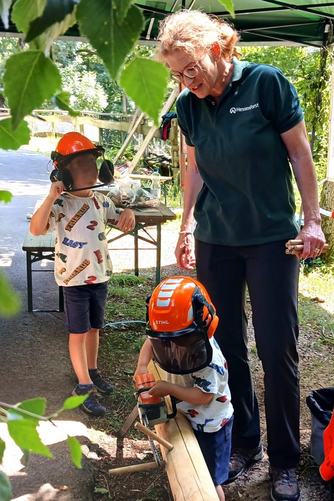 Eine Mitarbeiterin von HessenForst und zwei Kinder mit Spielzeugmotorsägen